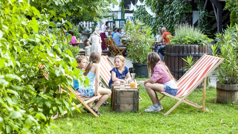 Kinder sitzen auf Liegest&uuml;hlen im Garten eines Caf&eacute;s.