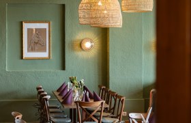 Gem&uuml;tlicher Essbereich mit Holztisch, St&uuml;hlen und geflochtenen Lampen.