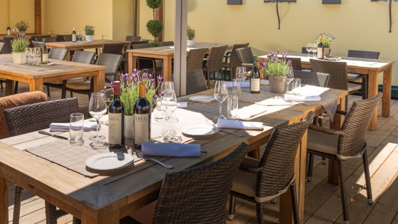 Eine Terrasse mit Holztischen, gedeckt mit Weinflaschen, Gl&auml;sern und Lavendel in T&ouml;pfen.