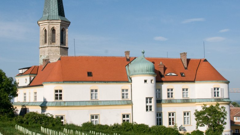 Schloss Gumpoldskirchen mit rotem Dach und Turm, umgeben von Weinbergen unter blauem Himmel.