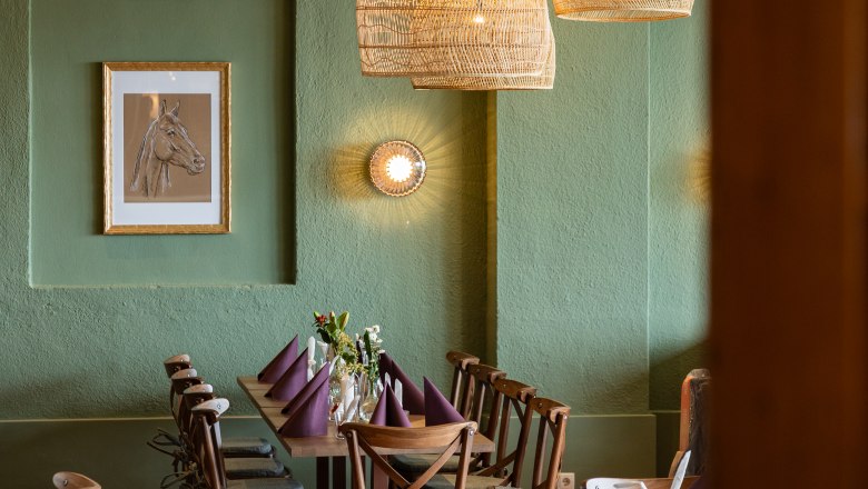 Gem&uuml;tlicher Essbereich mit Holztisch, St&uuml;hlen und geflochtenen Lampen.