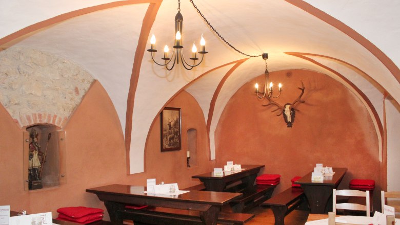 Rustikales Restaurant mit Gew&ouml;lbedecke, Holztischen und Hirschgeweih an der Wand.